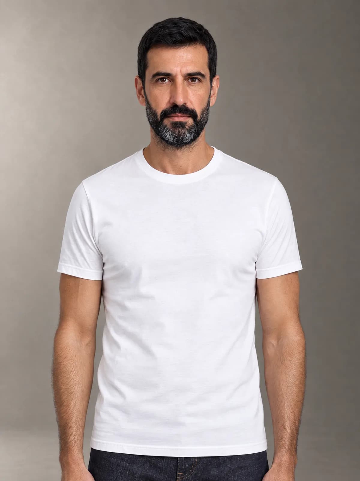 Javier in the white T-shirt and dark jeans, against a warm grey studio backdrop