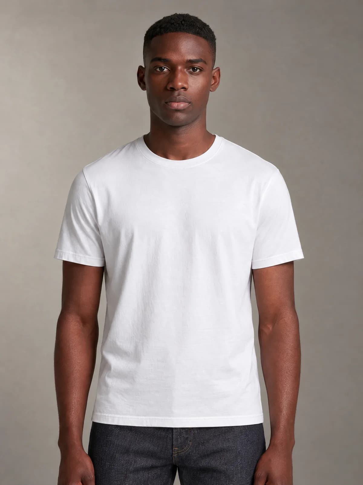 Mike in the white T-shirt and dark jeans, against a warm grey studio backdrop