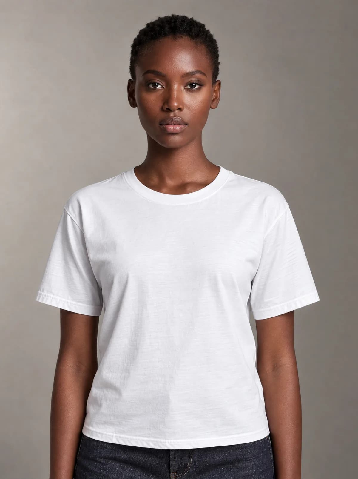 Zola in the white T-shirt and dark jeans, against a warm grey studio backdrop