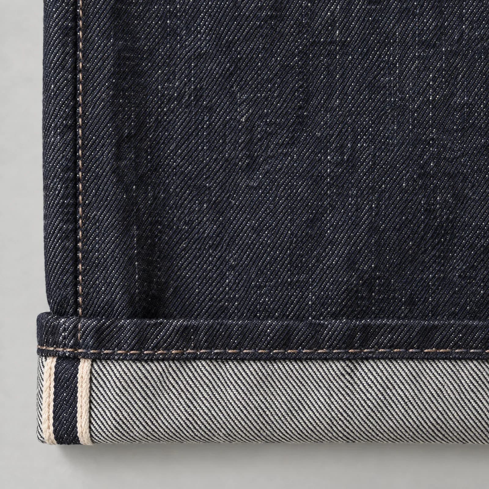 Detail of the DN01 straight jeans: raw indigo denim with a turned-up hem and selvedge edge