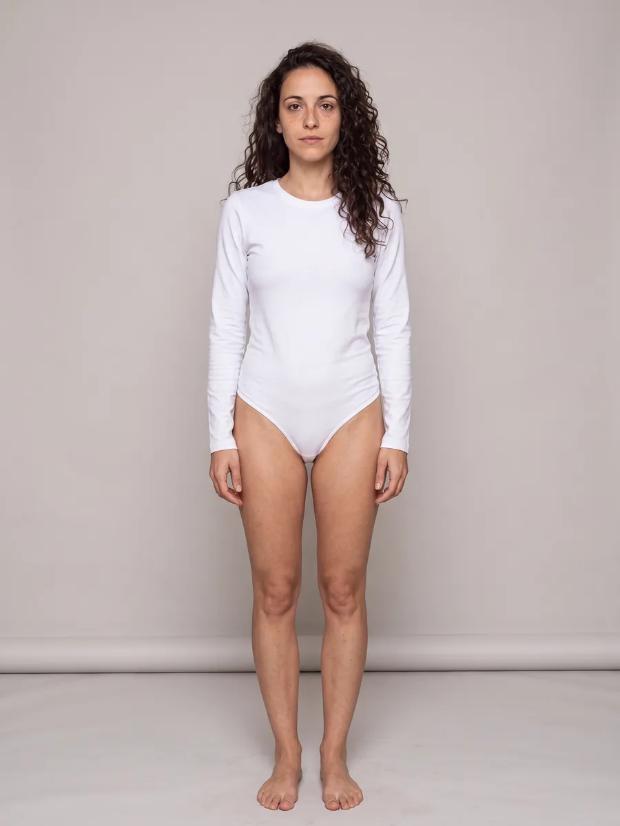 Dezelfde vrouw van top tot teen in een witte bodysuit, op blote voeten in een warmgrijze studio