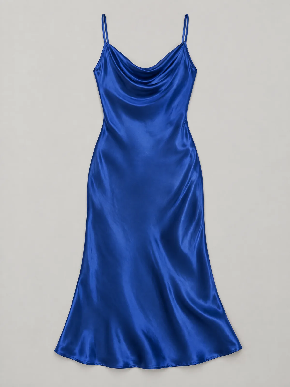Een kobaltblauwe satijnen slipdress plat gelegd op een lichtgrijze achtergrond